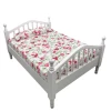 Lit miniature en bois blanc vu de trois quarts avec matelas fleuri